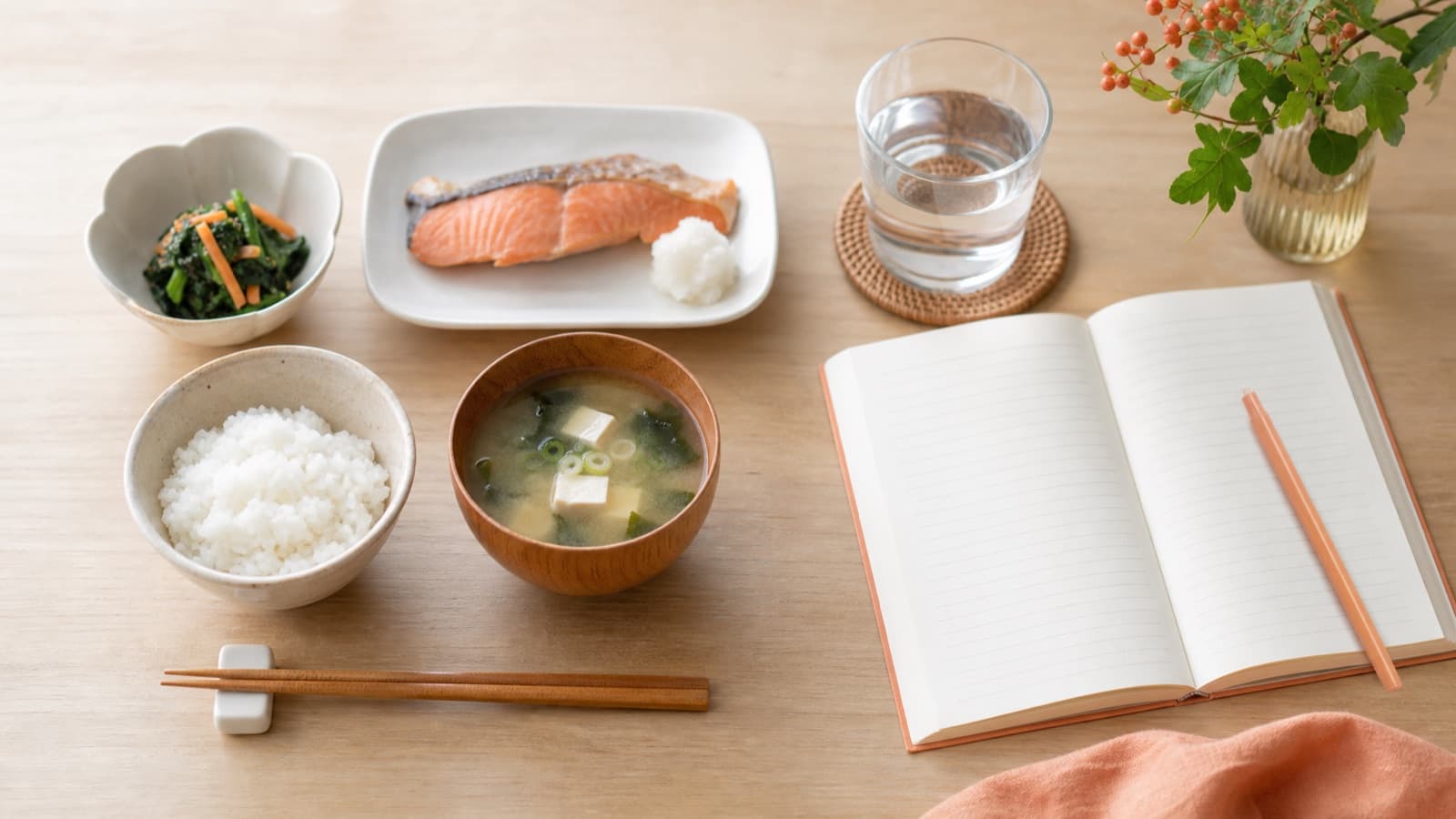 和食と水、食事の記録に使う開いたノートを並べた食卓